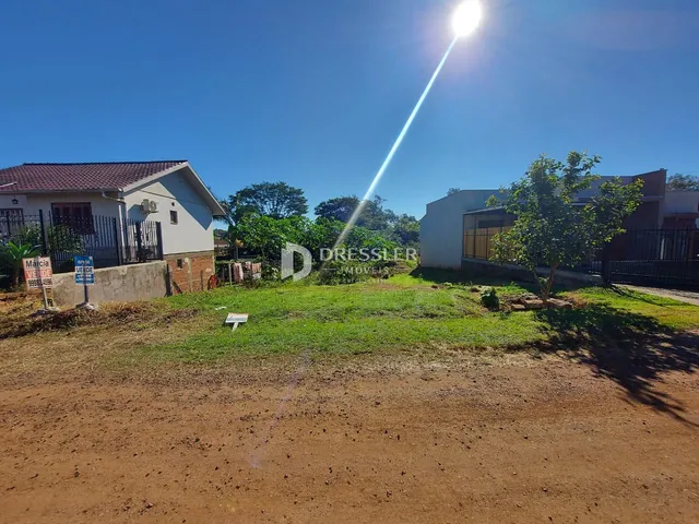 Vista externa de uma propriedade com gramado e construções ao fundo.