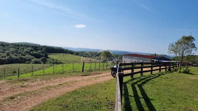 Vista de uma paisagem rural com campo verde e vegetação ao fundo.