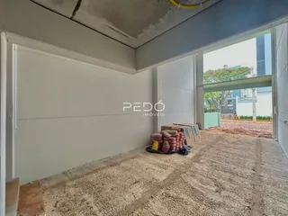 Vista interna de um espaço em construção com paredes brancas e piso de terra.