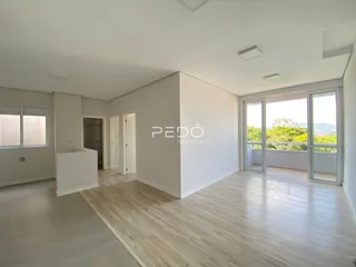 Ambiente interno de uma sala ampla com piso de madeira clara e portas de vidro.