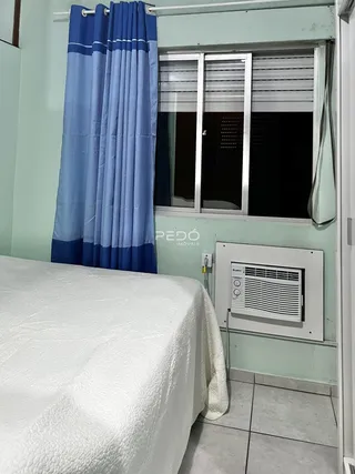 Quarto com cama coberta e janela com cortinas azuis.