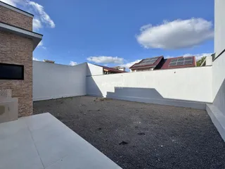 Vista externa de um pátio com piso de cascalho e parede branca.
