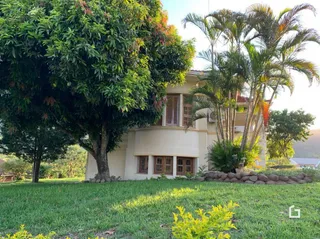 Vista externa de uma propriedade com gramado verde e vegetação densa.