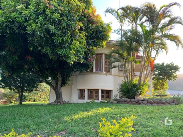 Vista externa de uma propriedade com gramado verde e vegetação densa.