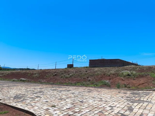 Vista da propriedade com terreno inclinado e estruturas ao fundo.