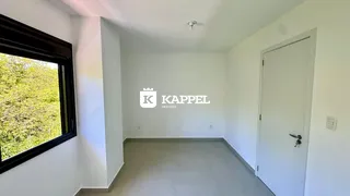 Foto de um cômodo interno com paredes brancas e uma grande janela mostrando vegetação externa.