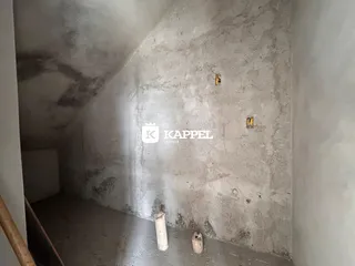 Foto interna de um corredor com paredes de concreto aparente e teto inclinado.