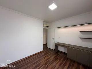 Foto do interior de uma sala com piso de madeira e parede branca.