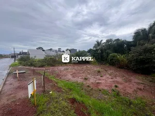 Vista externa de um terreno com solo avermelhado e vegetação rasteira sob um céu nublado.
