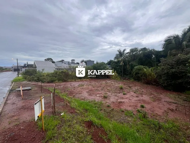 Vista externa de um terreno com solo avermelhado e vegetação rasteira sob um céu nublado.