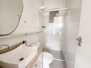 Banheiro com pia de granito e box de vidro transparente.