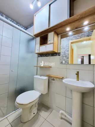 Foto interna de um banheiro com azulejos brancos e box de vidro.