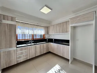 Vista interna de uma cozinha com armários e bancadas escuras.