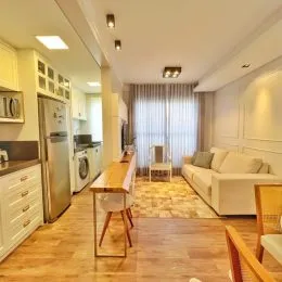 Foto interna de uma sala com piso de madeira e cortinas claras.