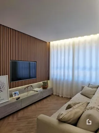 Sala de estar com painel de madeira e cortinas brancas.