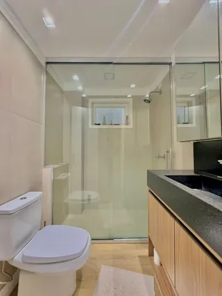Foto interna de um banheiro com box de vidro e piso de madeira clara.