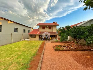 Vista externa de uma residência com jardim e área de terra batida.