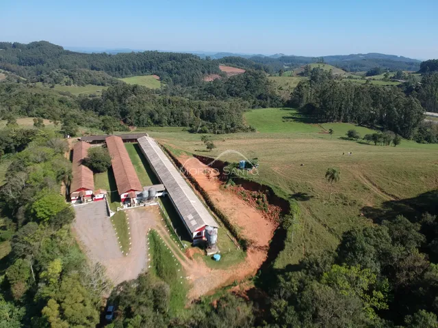 Vista aérea de uma propriedade rural com construções e áreas verdes em paisagem montanhosa.