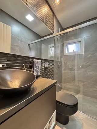Banheiro moderno com revestimento de azulejos escuros e box de vidro.