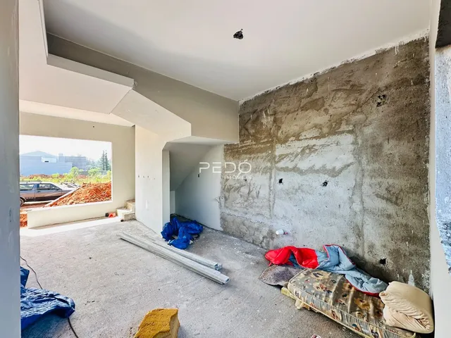 Espaço interno em obra com paredes expostas e materiais de construção no chão.