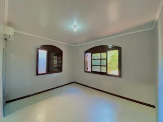 Uma foto de um cômodo interno com paredes brancas e janelas de madeira.