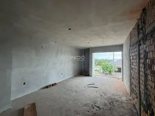 Imagem de um espaço interno vazio em construção com paredes brancas e piso de concreto.