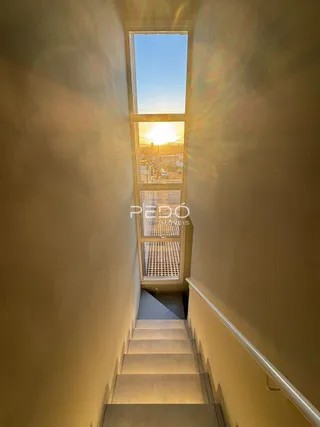 Vista de um corredor com escadaria iluminado por uma grande janela.