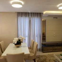 Foto interna de uma sala com cortinas claras e iluminação de teto.