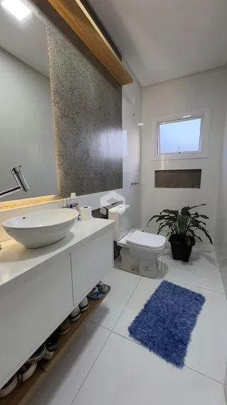 Banheiro moderno com pia de apoio e vaso sanitário em cerâmica branca.