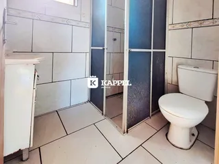 Uma foto interna mostra um banheiro com revestimento de azulejos brancos e um box de vidro.