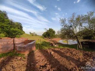 Vista de um terreno aberto com vegetação e um muro de tijolos.