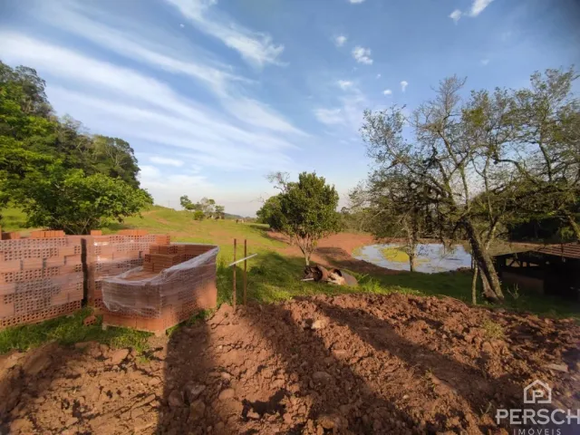 Vista de um terreno aberto com vegetação e um muro de tijolos.