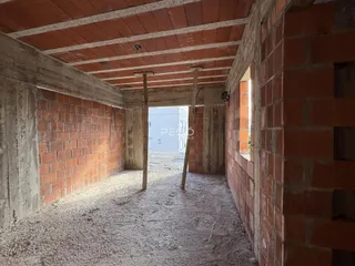 Interior de uma estrutura em construção com paredes de tijolo aparente e teto de concreto exposto.
