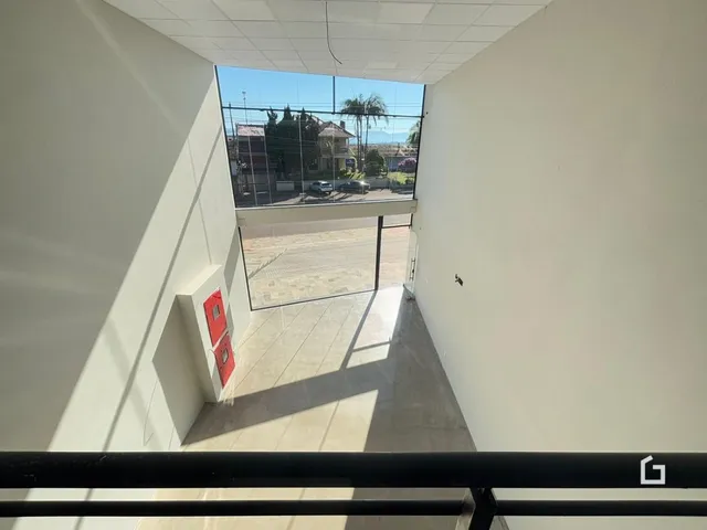 Vista de um corredor interno com portas vermelhas e grande janela de vidro.