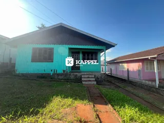 Fachada de uma casa azul-clara em Lajeado, Brasil, com trilhos de trem ao fundo.