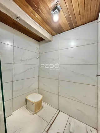 Foto interna de um banheiro com revestimento de azulejos brancos e teto de madeira.