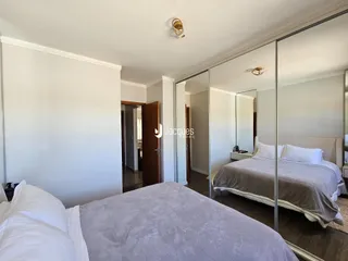 Quarto com cama grande e paredes brancas refletidas em espelho.