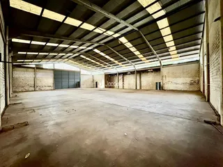 Espaço industrial amplo com teto de estrutura metálica e paredes de tijolo aparente.