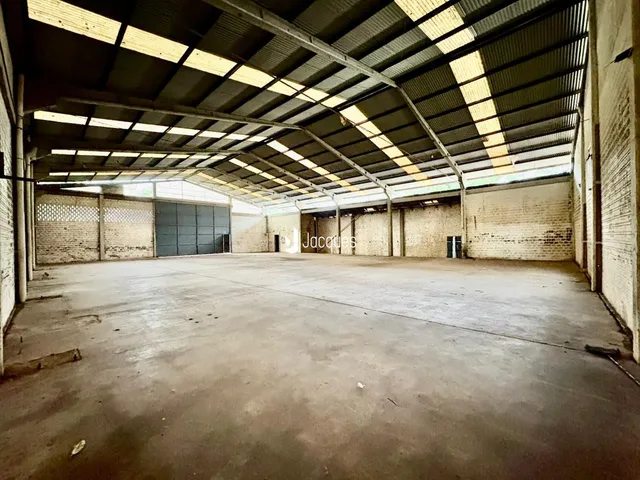 Espaço industrial amplo com teto de estrutura metálica e paredes de tijolo aparente.