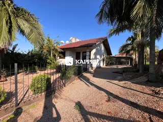 Foto da fachada de uma casa em Lajeado, Brasil, com vegetação e área de acesso de cascalho.