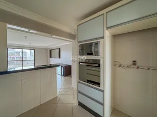 Interior de uma sala de estar com cozinha integrada e piso de cerâmica clara.