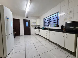 Vista interna de uma cozinha com armários brancos e piso cerâmico.