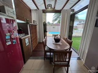 Mesa de jantar de madeira com cadeiras em uma área com vista para uma piscina externa.