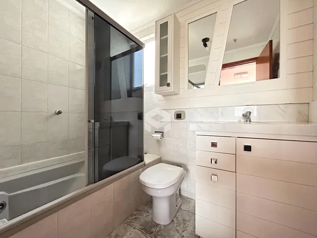 Interior de um banheiro com box de vidro e revestimento cerâmico.