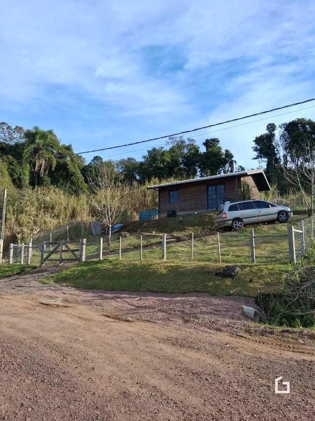 Vista externa de uma casa rural cercada por cerca e vegetação.