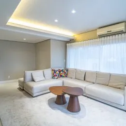 Sala de estar com sofá claro e cortinas brancas.