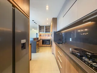 Vista interna de uma cozinha moderna com armários de madeira e bancadas escuras.