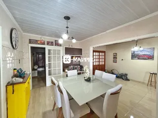 Sala de jantar com mesa grande e cadeiras brancas em um ambiente claro.