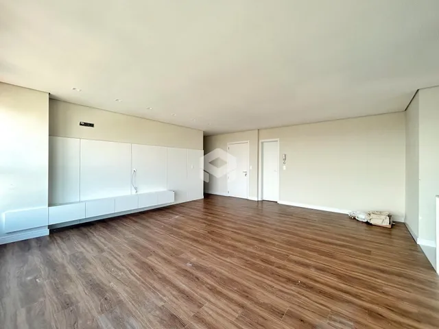 Interior de uma sala ampla com piso de madeira clara e armários embutidos.