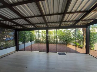 Vista interna de uma área coberta com piso de madeira e grandes janelas de vidro.